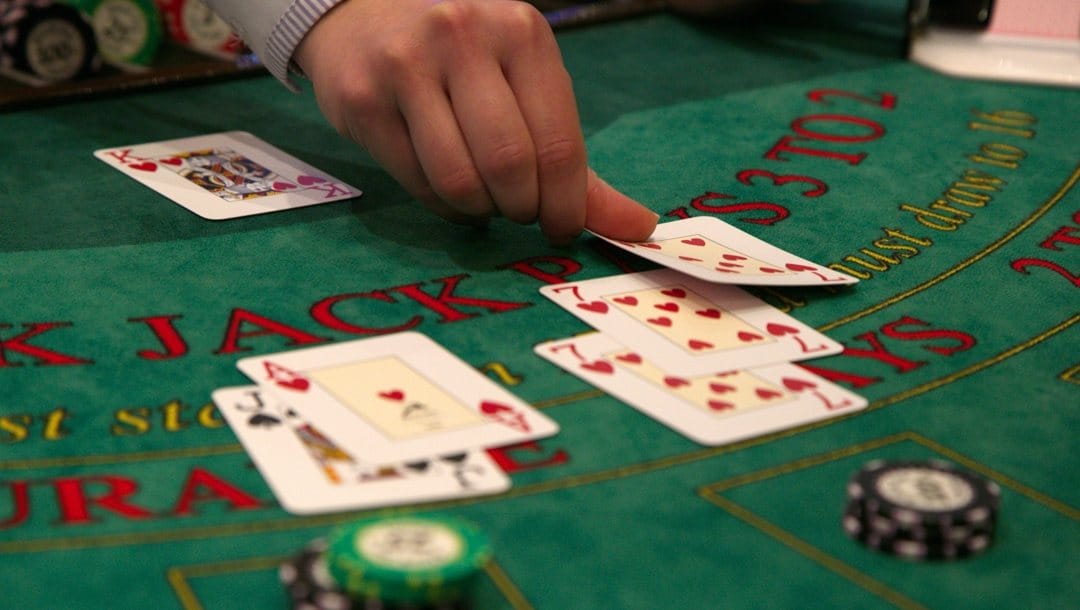 A croupier lays a seven of hearts on a green blackjack table in a casino