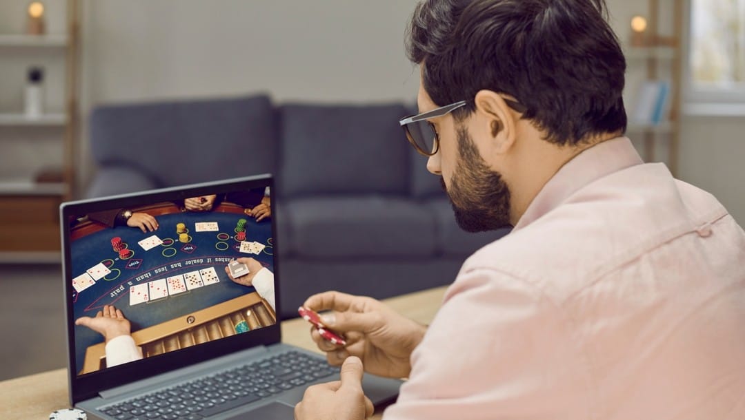 Man sits in front of laptop with poker chips playing online poker.
