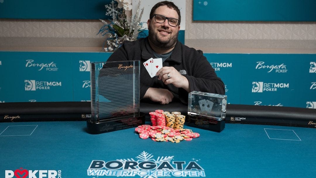 Alex Queen - Borgota Winter Poker Open Championship winner at a table with his trophy and winnings
