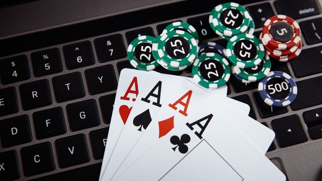 An Ace of Hearts, an Ace of Spades, an Ace of Diamonds, and an Ace of Clubs, placed on top of a laptop keyboard, with poker chips placed next to the cards.