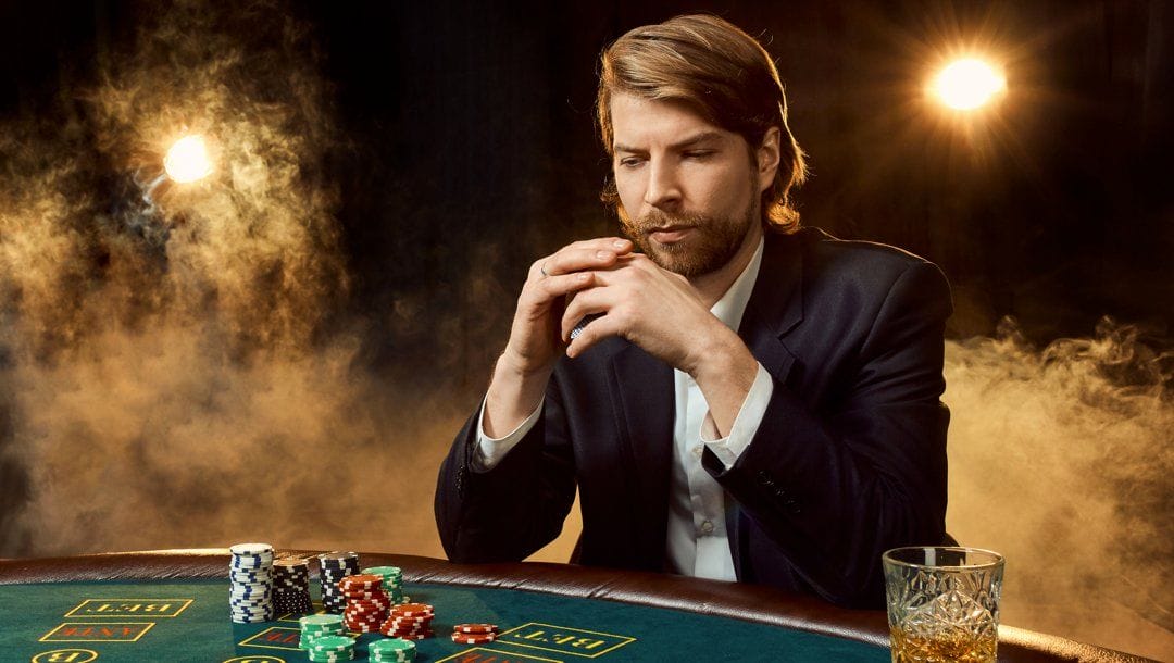 A person sits at a poker table holding their cards while looking at the table pensively.