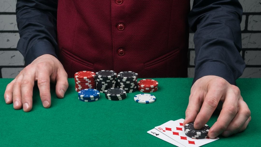 A casino dealer touching black casino chips and two playing cards.