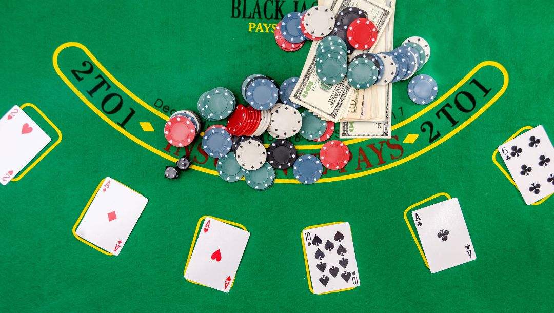 A blackjack table with cash, cards, and casino chips on it, as well as the words “2 to 1,” which are visible on either side of a rounded banner on the table.