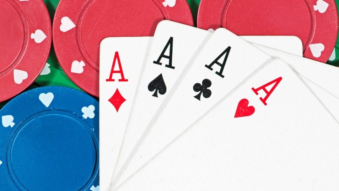 A close up shot of an Ace of Hearts, an Ace of Clubs, an Ace of Spades, and an Ace of Diamonds playing cards, neatly arranged on top of red and blue poker chips.
