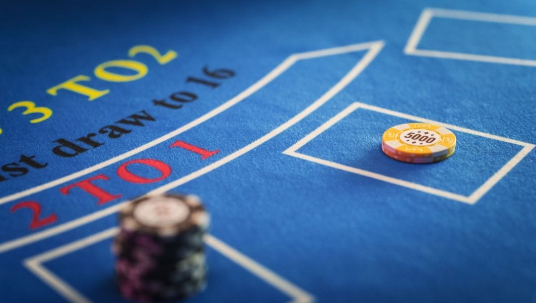 Closeup image of a yellow casino chip, and a stack of red casino chips on a bacarrat table.
