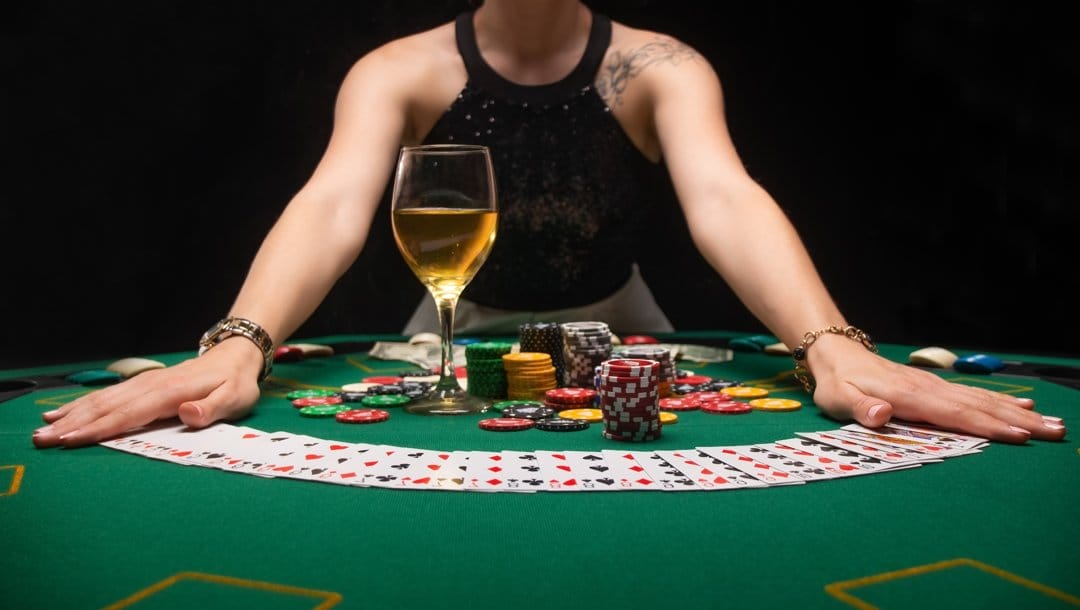 A dealer spreading out playing cards on a casino table. There are also casino chips and a wine glass on the table.