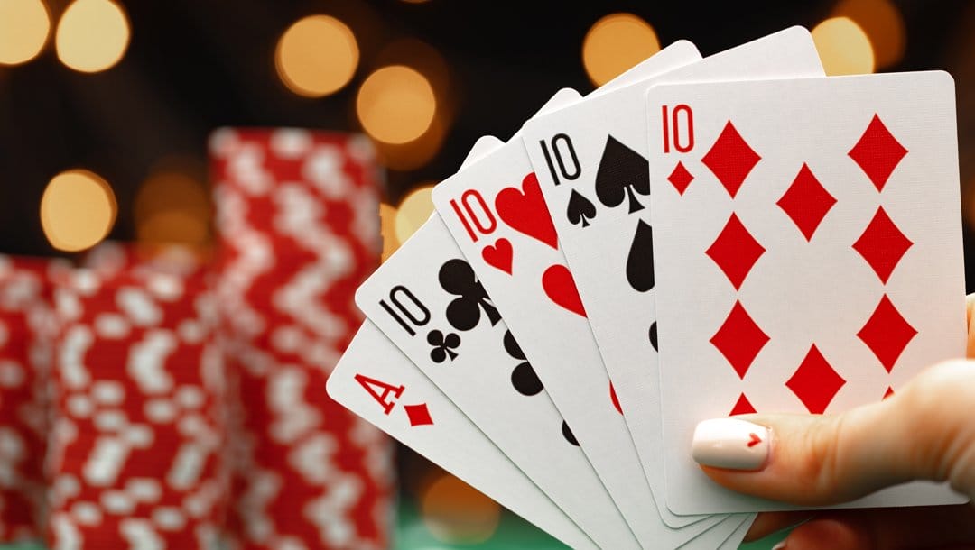 A person holding up a hand of cards. They are holding four 10s and an ace.