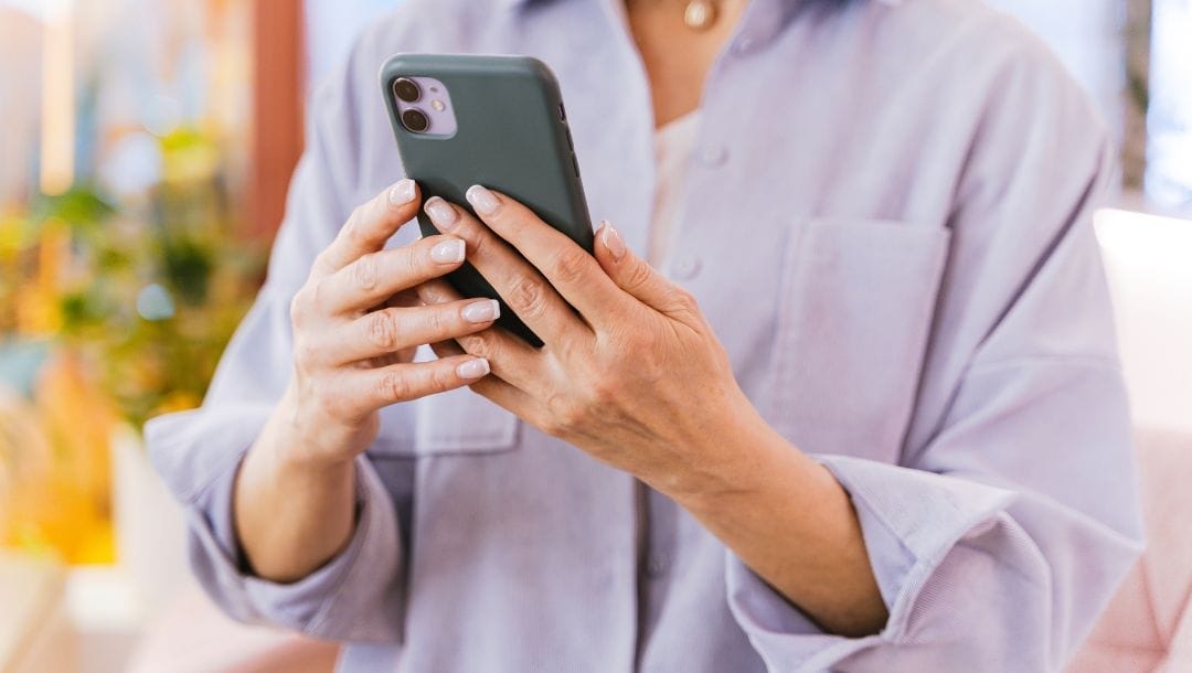 Woman looking at her phone, holding it with both hands.
