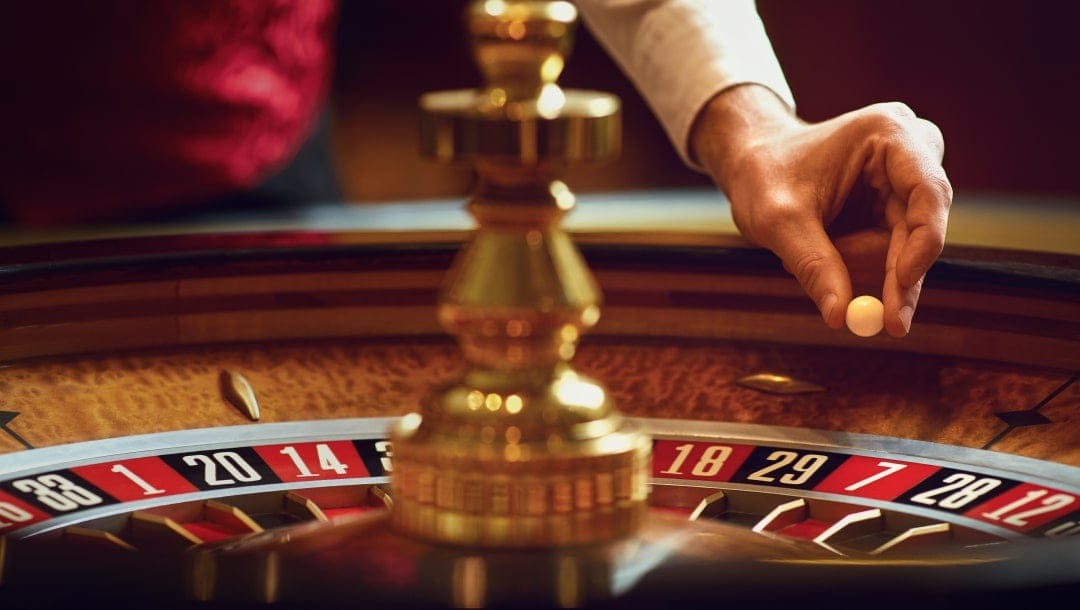 A roulette dealer about to drop a roulette ball into a roulette wheel.