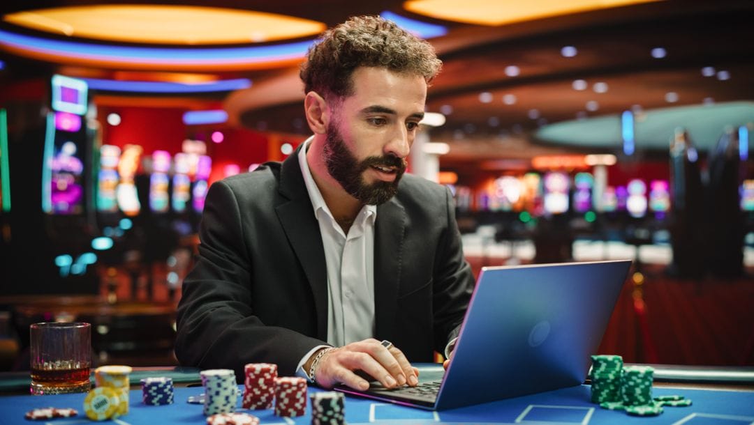 A person using their laptop at a casino game table. The laptop is surrounded by stacks of casino chips.