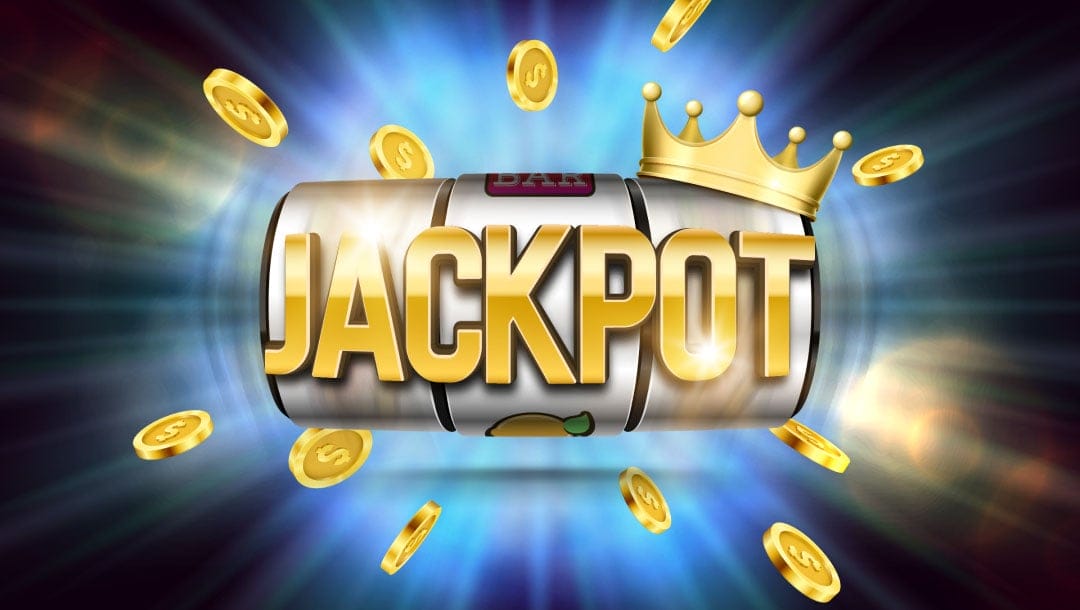 A slot reel with the word “jackpot” on it. It’s surrounded by flying gold coins and has a gold crown on the top right side of the reel.