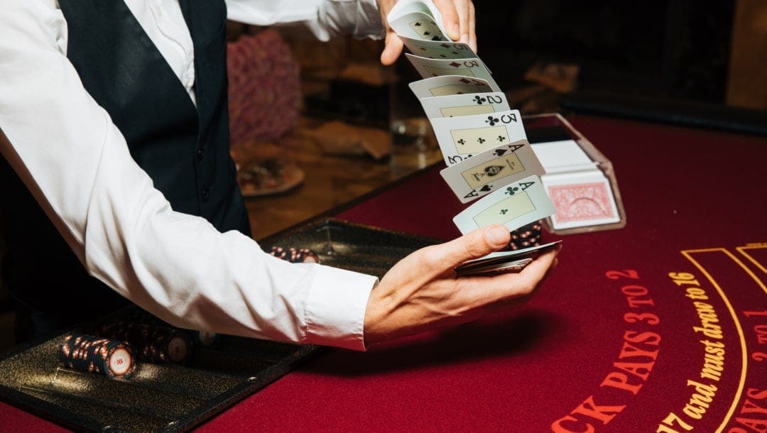 A blackjack dealer shuffling cards at a red blackjack table.