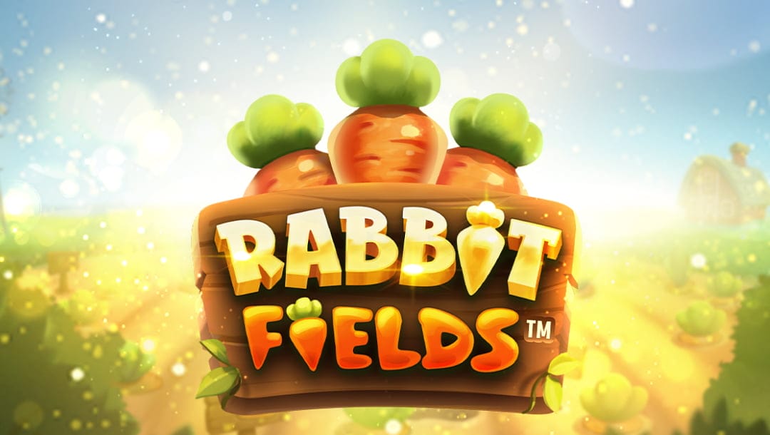 Rabbit Fields online slot logo in yellow and orange against a wooden board. There are three carrots above the wooden board. The background shows gold dust with green bushes and a white and blue sky.