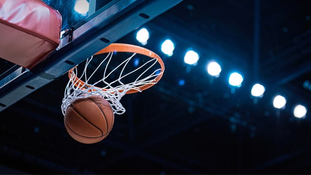A basketball going through the net of a basketball hoop in a stadium.