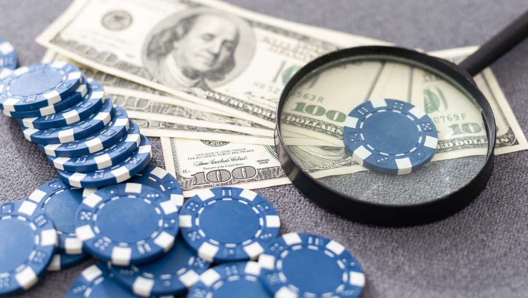 Blue poker chips next to four $100 bills; One poker chip is on top of the bills with a magnifying glass on top of it.
