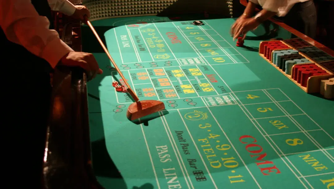 A photograph of a craps table in a casino with a player getting ready to place their bets on one side of the table and a Stickman holding the craps stick (or mop) on the other.