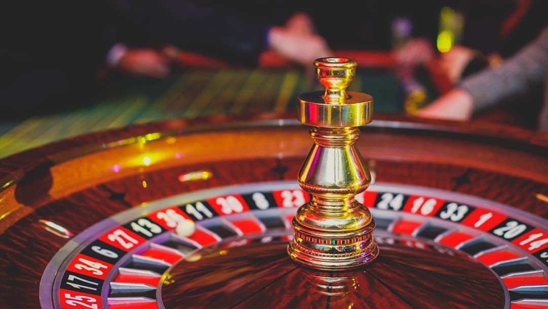 Roulette wheel with players in the background. The roulette table is green.