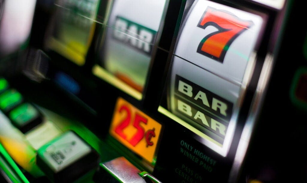 A slot machine with classic symbols such as the bar and the red number seven. There is a 25c sign below the reels. The slot machine is black and silver.