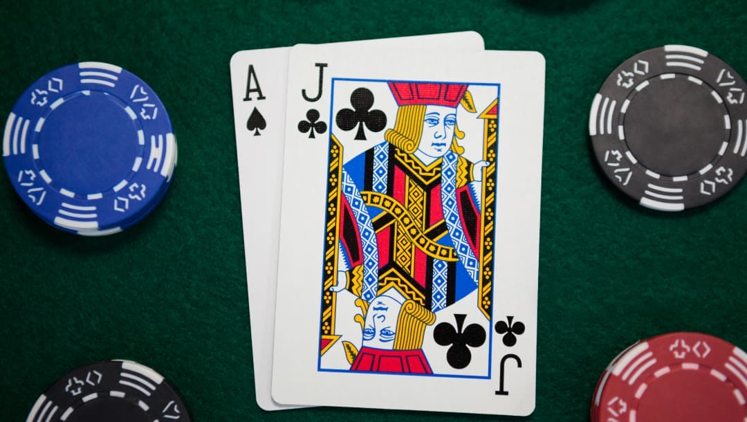 A jack of clubs and an ace of spades sitting on a green casino table. There are four small stacks of casino chips around it.