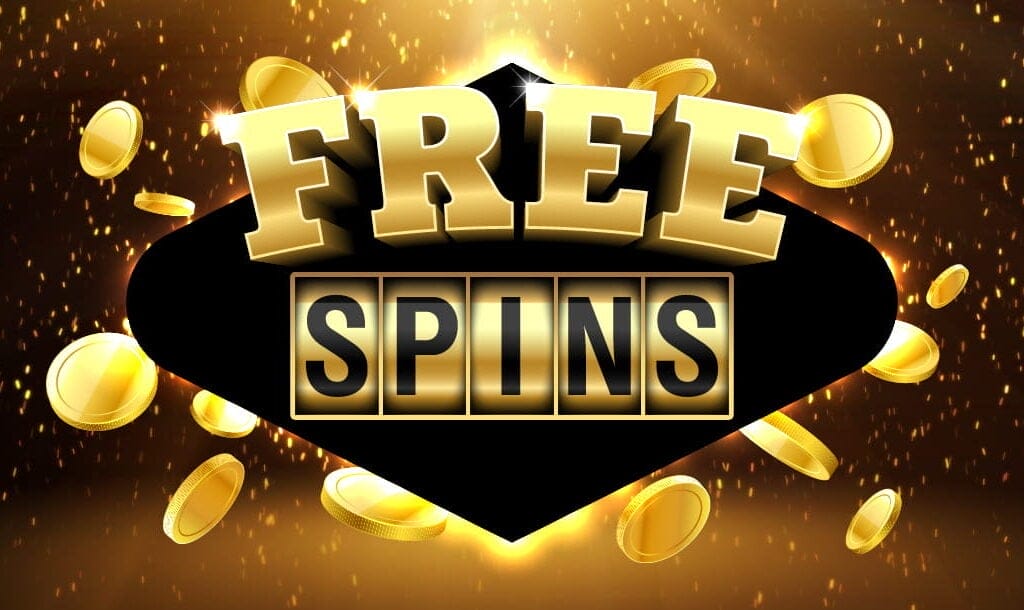 A concept image for bonus spins in online slot games. The word “Free” is spelled out in bold, golden letters and appears on top of the word “Spins” spelled out across the reels of a slot game. The words have a black diamond behind them, to separate them from the background, which is made up of gold coins and sparks on a dark backdrop.