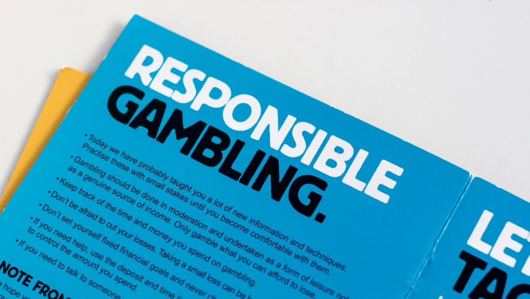 A photograph of a blue pamphlet on a white table. The pamphlet has the words “Responsible Gambling” written in bold, capital letters at the top as well as a few summary points and tips for responsible gamling below it.