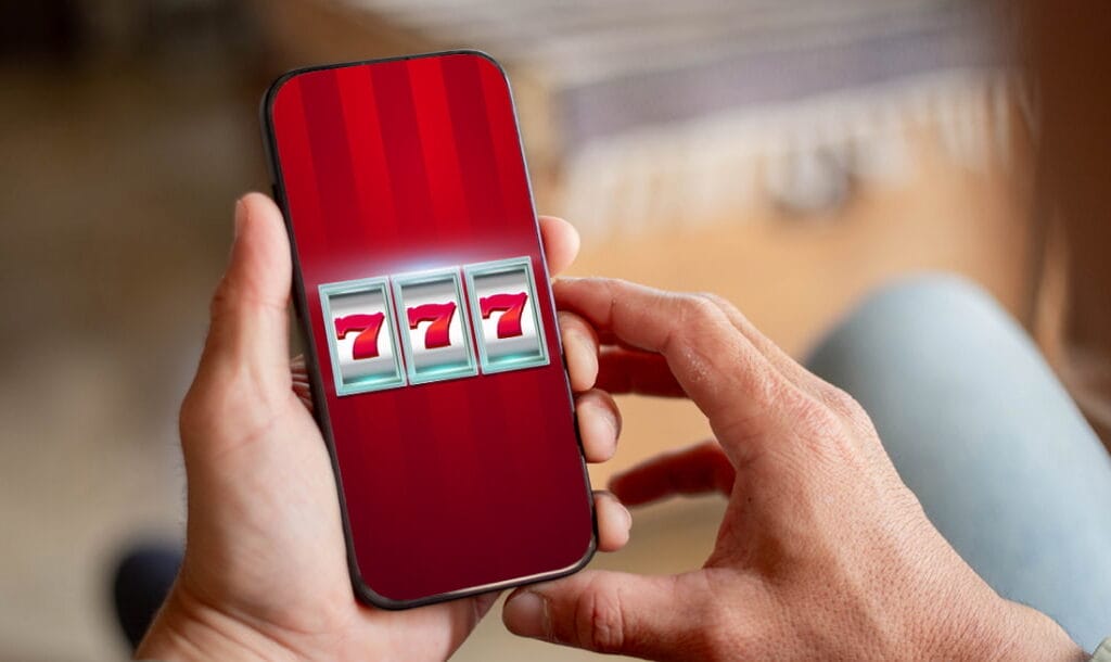 A person holding a smart phone with slot reels on it. There are three red 7s on the slot reels.