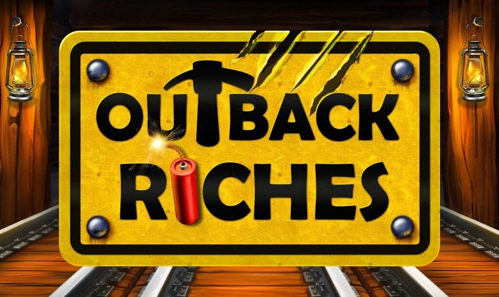 The Outback Riches slot title screen. The background is a mineshaft with railway tracks. In the foreground is a construction sign with the game’s title. A stick of dynamite is in place of the “i” in the word “riches.”